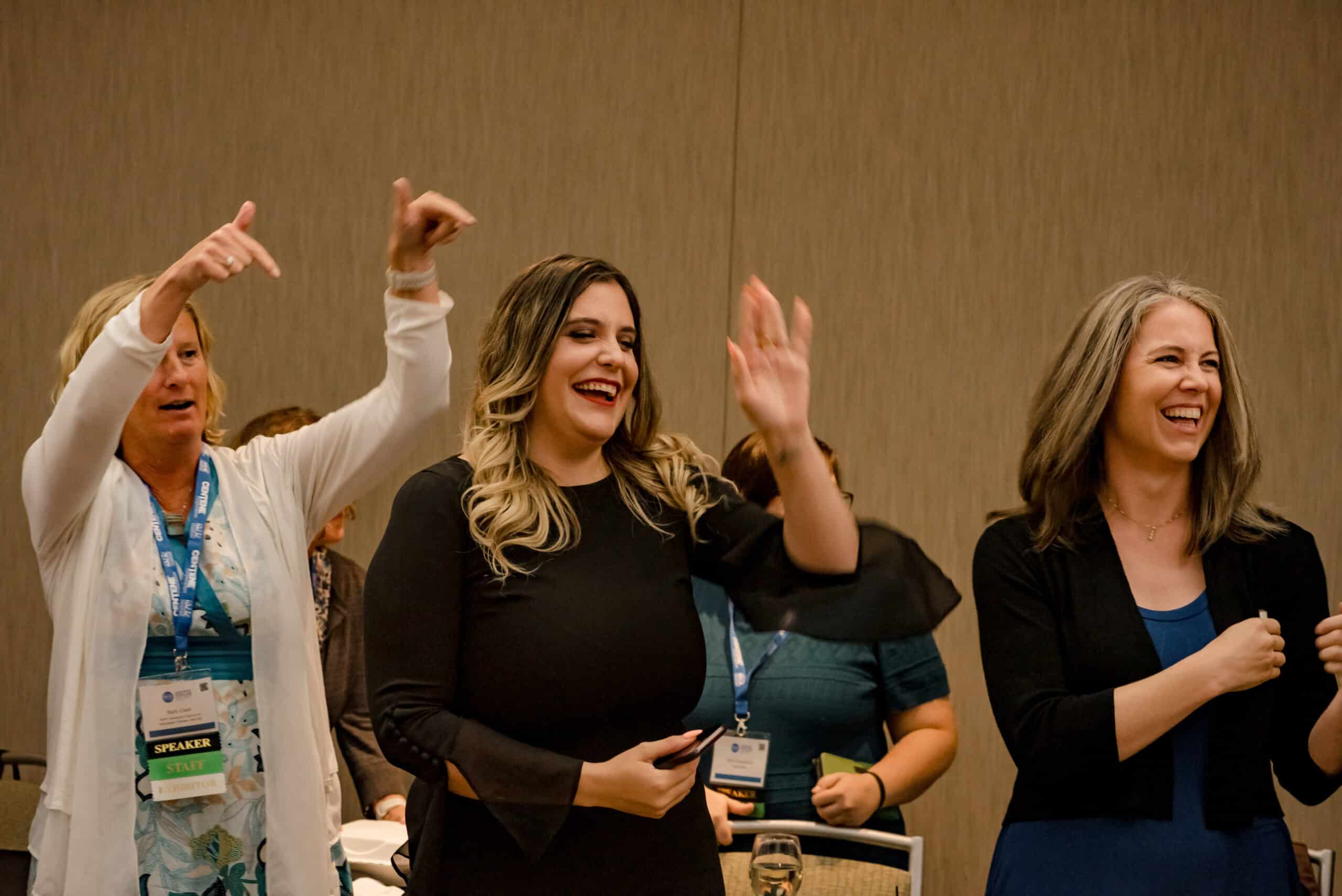 Three people standing up, smiling, and with their hands in the air in a conference room.