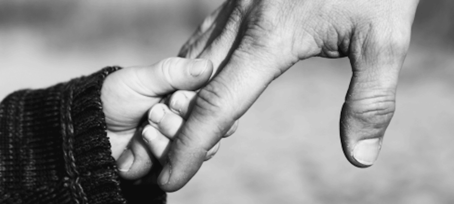 1 A black and white photo of a small child's hand holding the finger of a larger adult hand