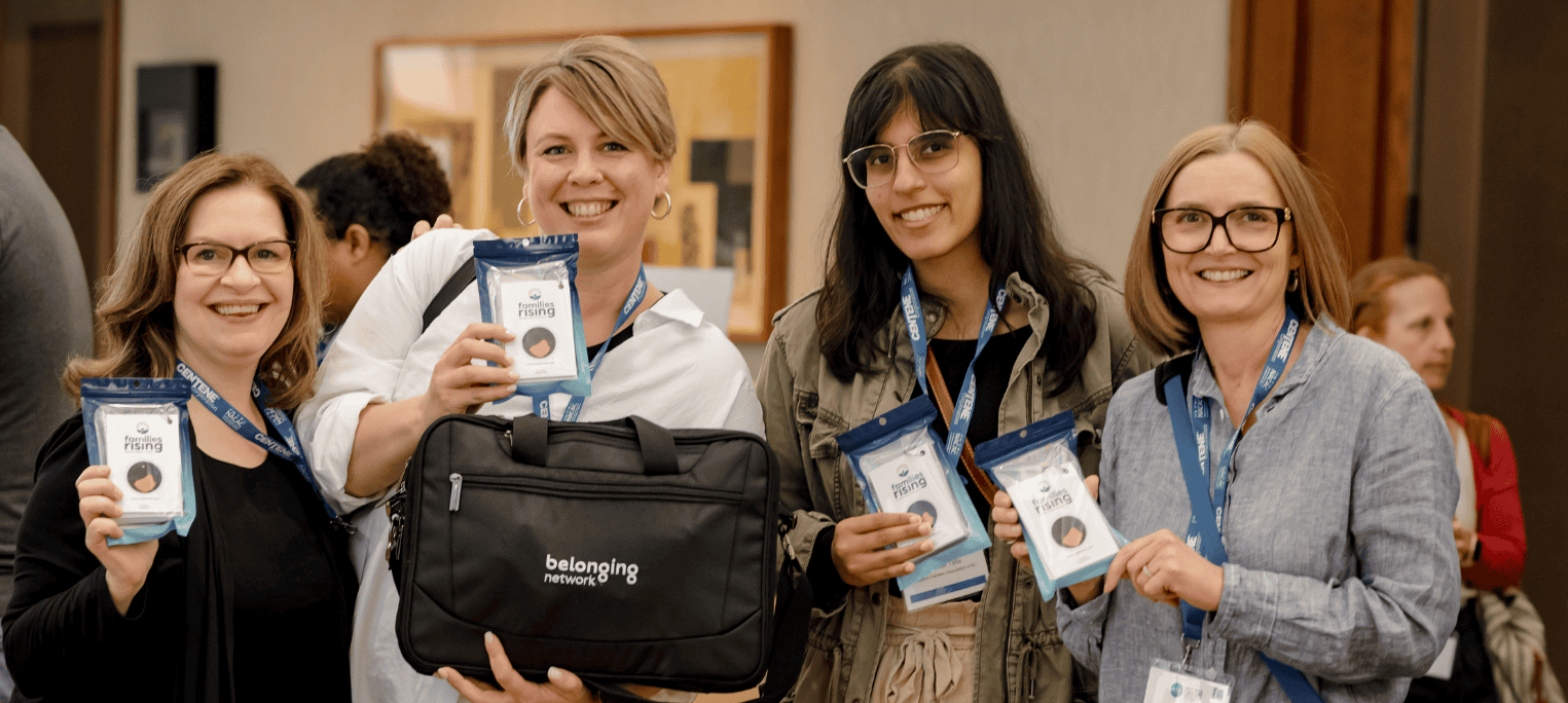 5 Four female conference attendees smiling at the camera and holding Families Rising card packs
