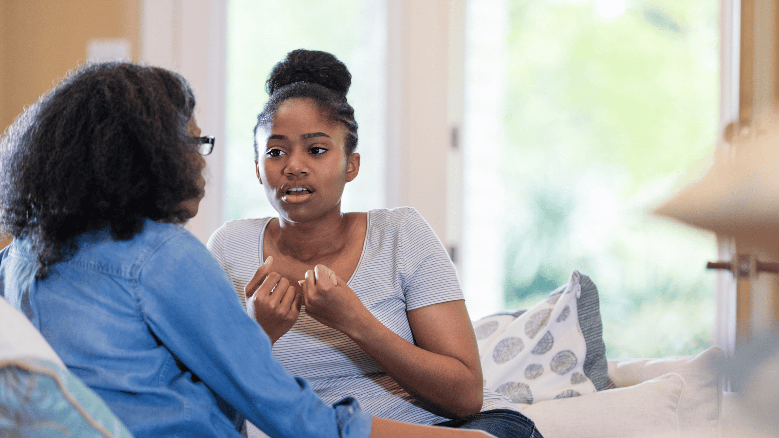 A teenage girl talking to an older woman while sitting on the couch