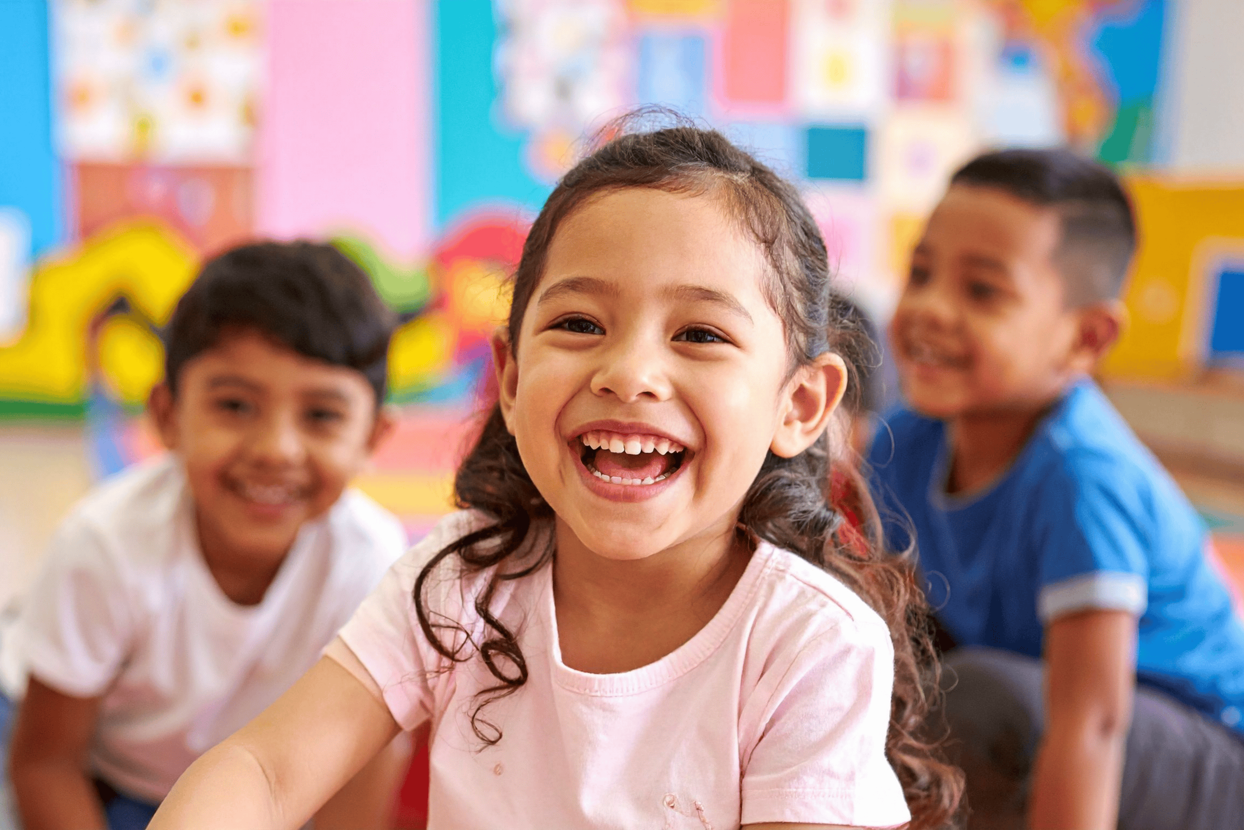 A young Latinx girl smiles at the camera, the background suggesting she's in a school setting