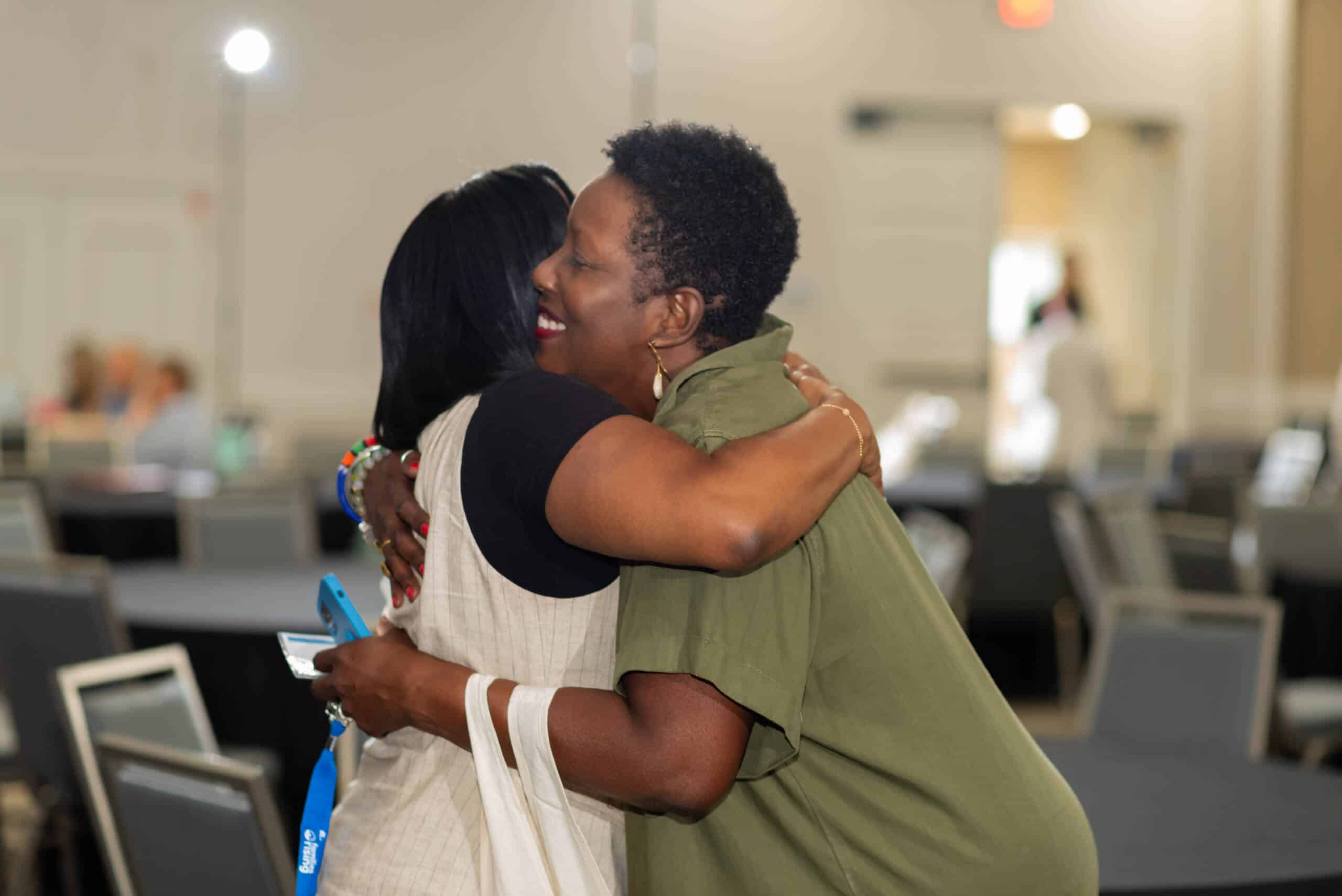 Two people greet each other and hug in a conference room